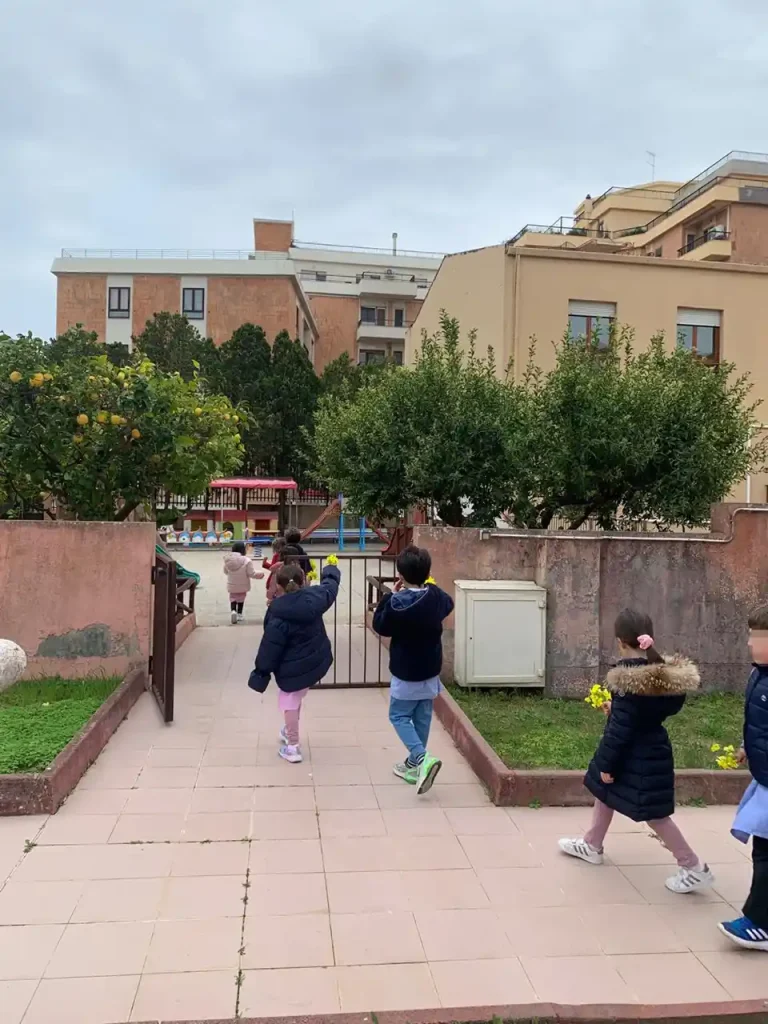 Bambini attraversano il giardino della scuola durante un'attività educativa all'aperto.