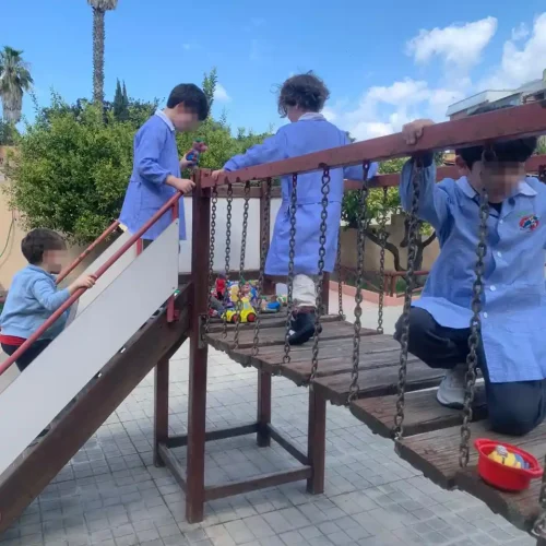 Bambini giocano sul ponte sospeso dell'area giochi esterna della scuola dell'infanzia.