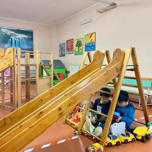 Bambini giocano nell'area interna attrezzata con scivoli e giochi educativi della scuola dell'infanzia.