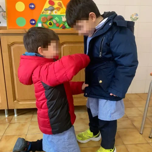 Due bambini si aiutano a indossare il giubbotto durante una routine quotidiana nella scuola dell'infanzia.